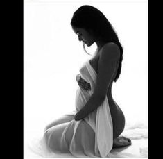 a pregnant woman sitting on top of a bed wearing a white dress and holding her stomach