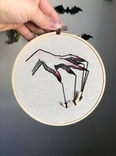 someone is holding up a small embroidery project with bats in the background and one hand on it