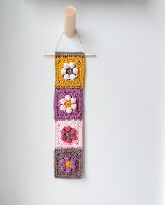 a crocheted wall hanging with flowers on the top and bottom, attached to a hook