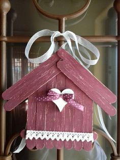 a pink birdhouse hanging from a wooden frame with white lace on the top and bottom