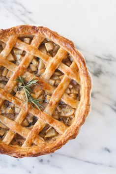 an apple pie with a sprig of rosemary on top sits on a marble surface