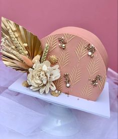 a pink hat with gold feathers and flowers on top of a white stand against a pink background