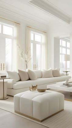 a living room with white furniture and large windows in the back ground, there is a coffee table on one side of the couch