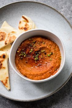 a white plate topped with a bowl of hummus and tortilla wedges