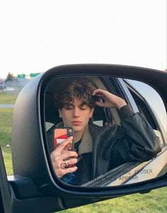 a young man taking a selfie in the side view mirror of a car with his cell phone