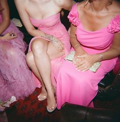 two women in pink dresses sitting next to each other at a formal event, one holding a purse