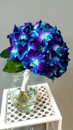 a vase filled with blue flowers sitting on top of a white table next to a wall