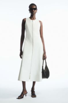 The COS womenswear team know the importance of having a staple dress or two in your wardrobe. This off-white style is crafted from a cotton blend and cut with a fitted bodice that cascades down to a subtly flared midi skirt. The modern zip gives it a laid-back ease; match your jewellery to the silver-tone hardware.  Slim fitSleeveless  65% Cotton, 28% Polyamide (Nylon), 7% Elastane / Machine wash Back length of size S is 122.2cm / Model wears a size S Cos Outfit, 2024 Clothes, Normcore Fashion, Flared Midi Skirt, Staple Dress, Midi Flare Skirt, Seersucker Dress, White Midi Dress, White Outfits