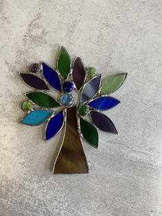 a multicolored tree brooch sitting on top of a white table next to a wall