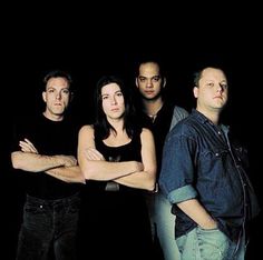 four people standing in front of a black background with their arms crossed and looking at the camera