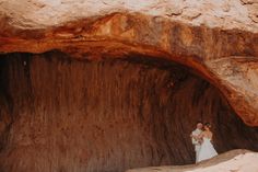 two people standing in the middle of a cave with rocks on either side and one person wearing a white dress