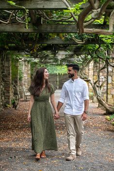 a man and woman holding hands while walking through an archway in the park with trees on either side