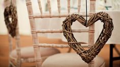 a heart shaped wicker chair hanging from the back of a wooden chair in front of a table