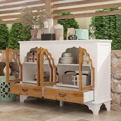 a white cabinet with wooden doors and drawers in a room filled with pots and plants