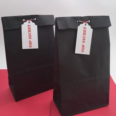 two black paper bags with red and white tags on them, sitting on a pink surface