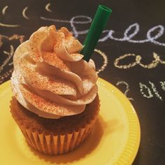 a cupcake with frosting and a green straw in it on a yellow plate