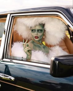 a woman with green makeup and white feathers sitting in the back seat of a car