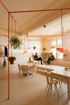 two people sitting on benches in a room with plants hanging from the ceiling and windows