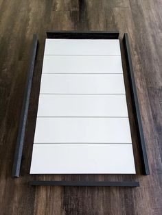 a wooden floor with a white board and black frame on it, next to a bottle of wine