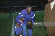 a man kneeling down next to a young boy holding a soccer ball on top of a field