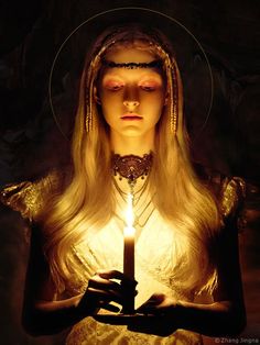 a woman holding a candle in her hands with the light shining on her face and head