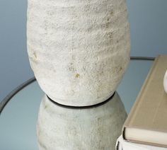 a white vase sitting on top of a glass table next to a stack of books