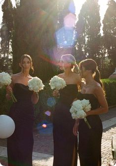 three bridesmaids in black dresses holding white bouquets and balloons with the sun shining on them