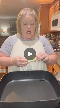 a woman in an apron holding a pan with food inside it and making a funny face