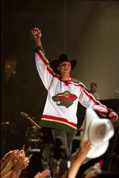 a man on stage with his arms in the air and one hand raised up as he sings