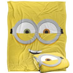 a yellow blanket with two eyes and one eyeball on the front, is next to a pillow