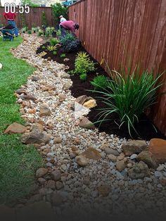 a garden with rocks and plants next to a fence