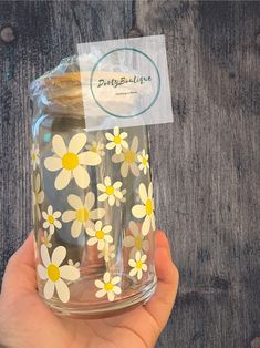 a hand holding a glass with yellow and white daisies on the bottom, in front of a wooden background