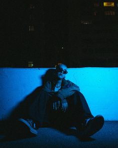 a man sitting on the ground in front of a wall at night with his eyes closed