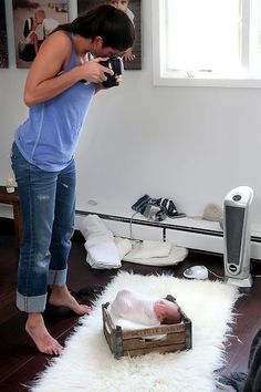 a woman taking a photo of a baby in a box on top of a rug