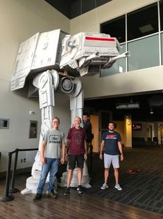 three men standing in front of a giant model of a star wars at - at