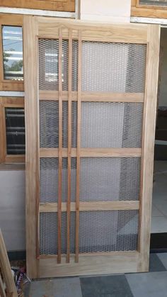 a wooden door with mesh panels on the side and windows in the back ground behind it