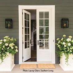 two white planters filled with flowers on the outside of a door way to a house