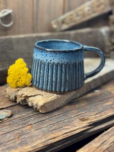 a blue mug sitting on top of a wooden table next to a small yellow flower