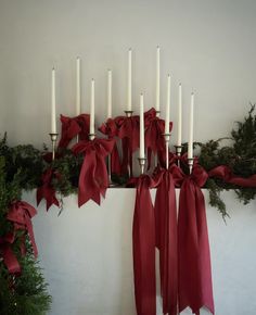 a bunch of white candles with red bows on them next to evergreen branches and greenery