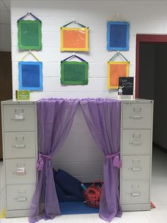 an office cubicle with purple curtains and pictures hanging on the wall above it's doors