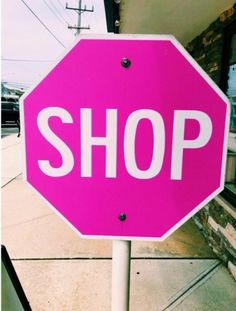 a pink stop sign sitting on the side of a road next to a store front