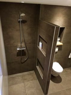 a bathroom with a walk in shower next to a white toilet and brown tiled walls