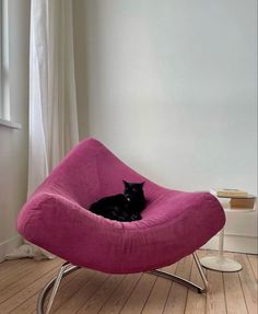 a black cat is sitting in a pink chair