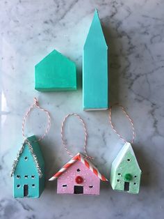 three wooden houses are hanging from twine strings on a marble surface, one is green and the other is pink