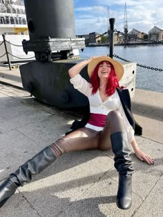 a woman sitting on the ground with her legs crossed wearing boots and a wide brimmed hat