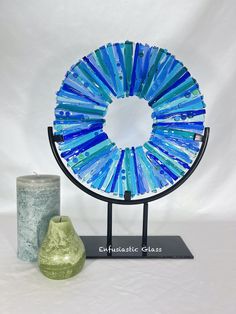 a blue and green vase sitting next to a circular glass sculpture on a stand with a white background