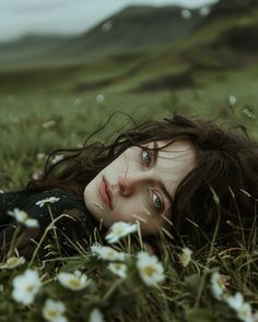 a woman laying in the grass with daisies around her neck and eyes wide open