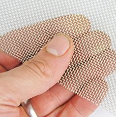 a hand holding a piece of metal mesh on top of a white cloth covered surface