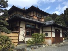 an old japanese style house with wood trimmings on the roof and windows, surrounded by trees