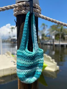 a blue crocheted bag hanging from a wooden pole next to water and boats